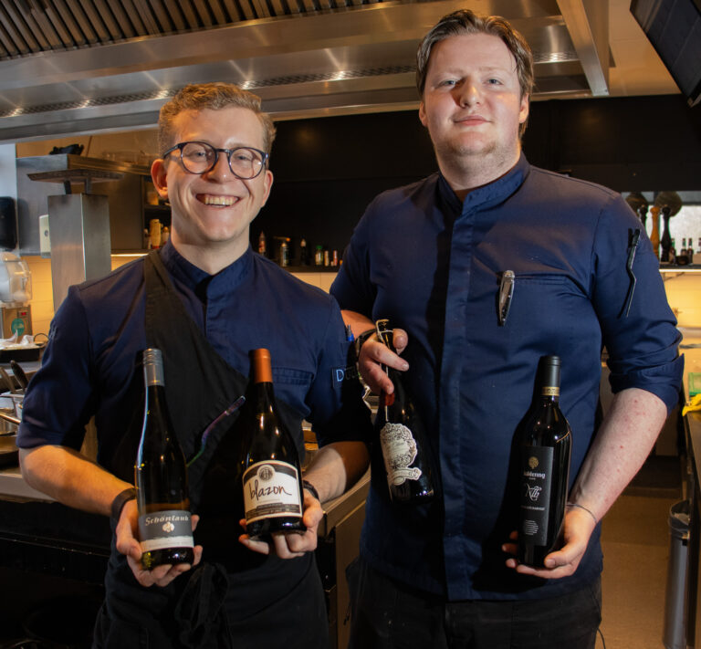 twee leerling koks met wijnflessen in de hand