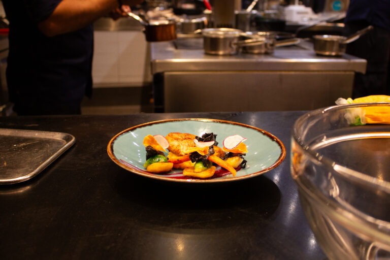 Bordje met een gerecht met garnaal met de keuken op de achtergrond